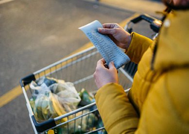 Some looking at grocery receipt standing over cart in parking lot