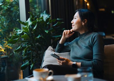 Young Woman With Smartphone Looking Out Cafe Window