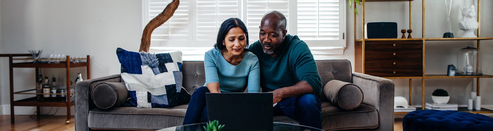 Couple at home on couch looking a laptop on coffee table